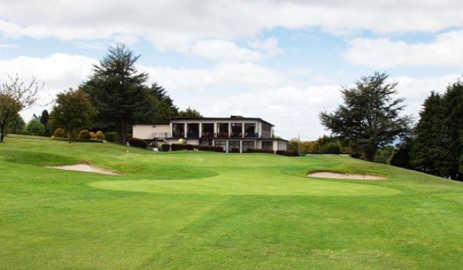 Mallow Golf Club clubhouse and its balcony seen from the fairway, with bunkers guarding the green below